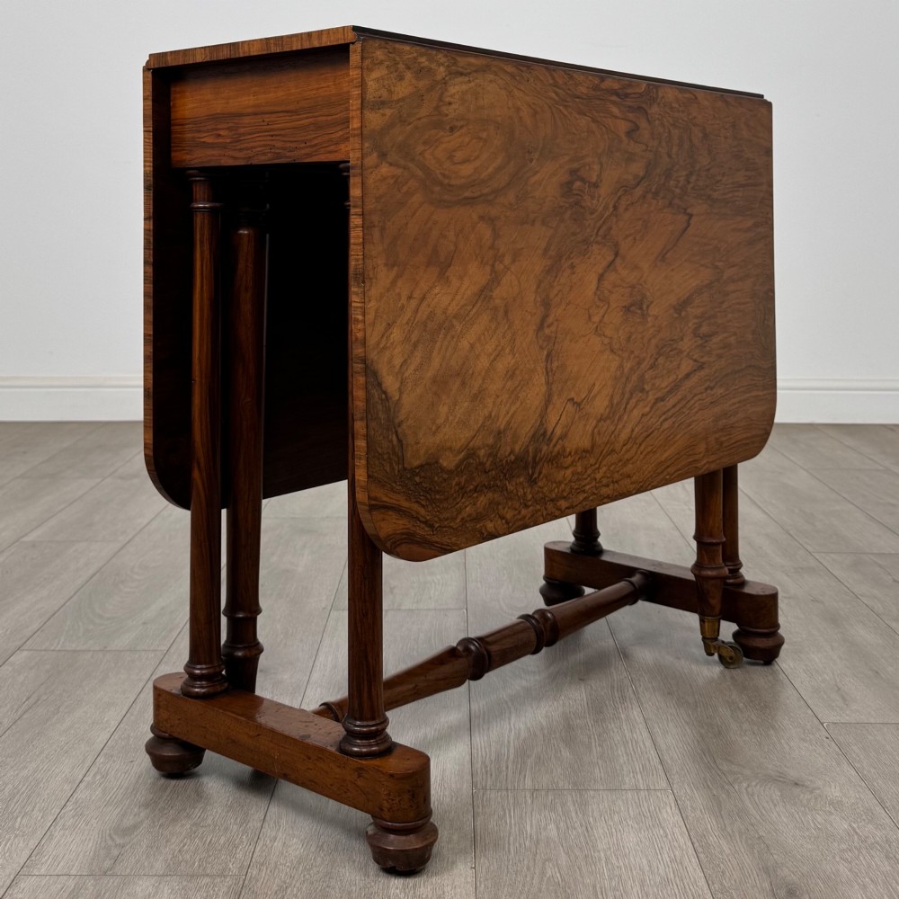 A 19th-century Victorian Sutherland table crafted from burr walnut with two folded drop leaves, turned supports, and brass castors.