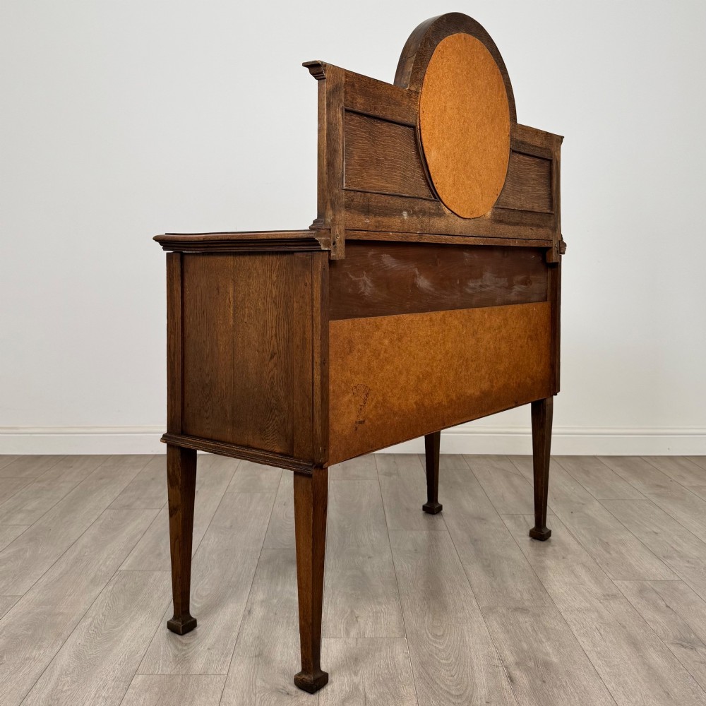 An Edwardian oak sideboard featuring a raised gallery back with a central circular mirror, a left cupboard door, two right drawers, and brass drop handles. View V