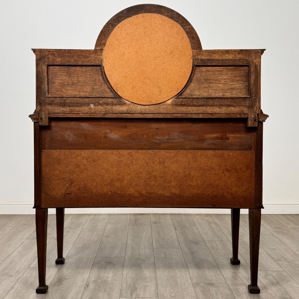 An Edwardian oak sideboard featuring a raised gallery back with a central circular mirror, a left cupboard door, two right drawers, and brass drop handles. View VI