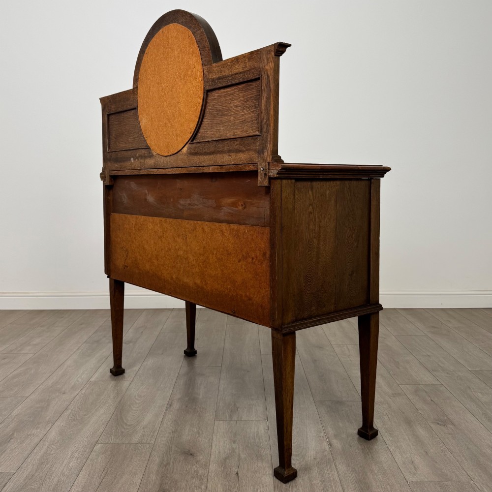 An Edwardian oak sideboard featuring a raised gallery back with a central circular mirror, a left cupboard door, two right drawers, and brass drop handles. View VII