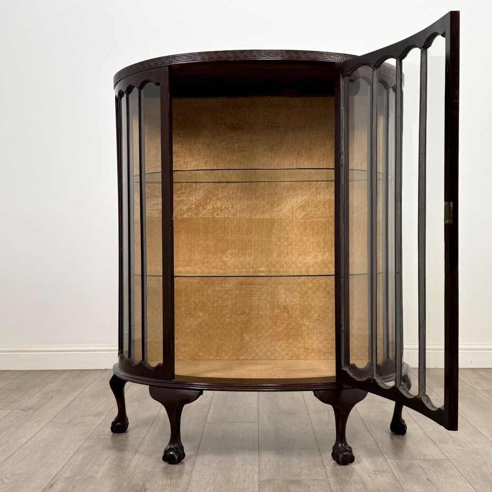 An Edwardian dark mahogany demi-lune display cabinet featuring glazed curved panels, a carved Greek key frieze, glass internal shelves, and cabriole legs with ball-and-claw feet. View II