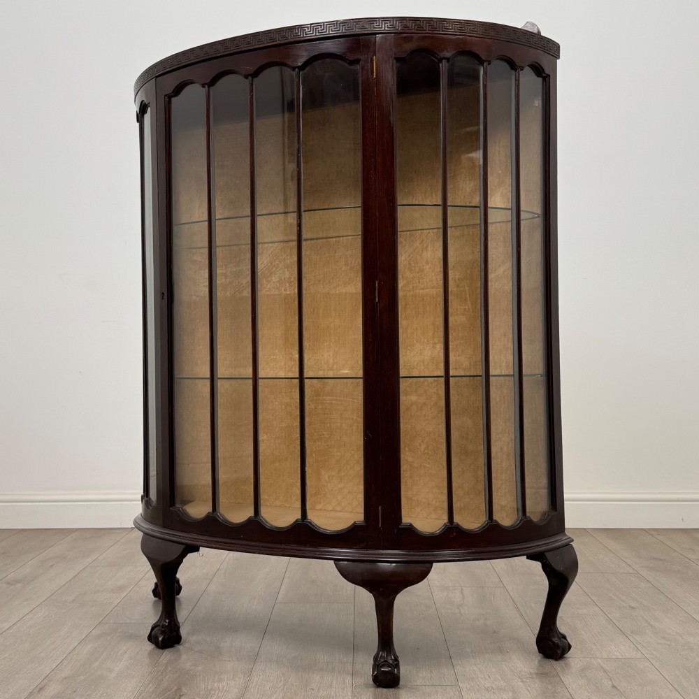 An Edwardian dark mahogany demi-lune display cabinet featuring glazed curved panels, a carved Greek key frieze, glass internal shelves, and cabriole legs with ball-and-claw feet. View III
