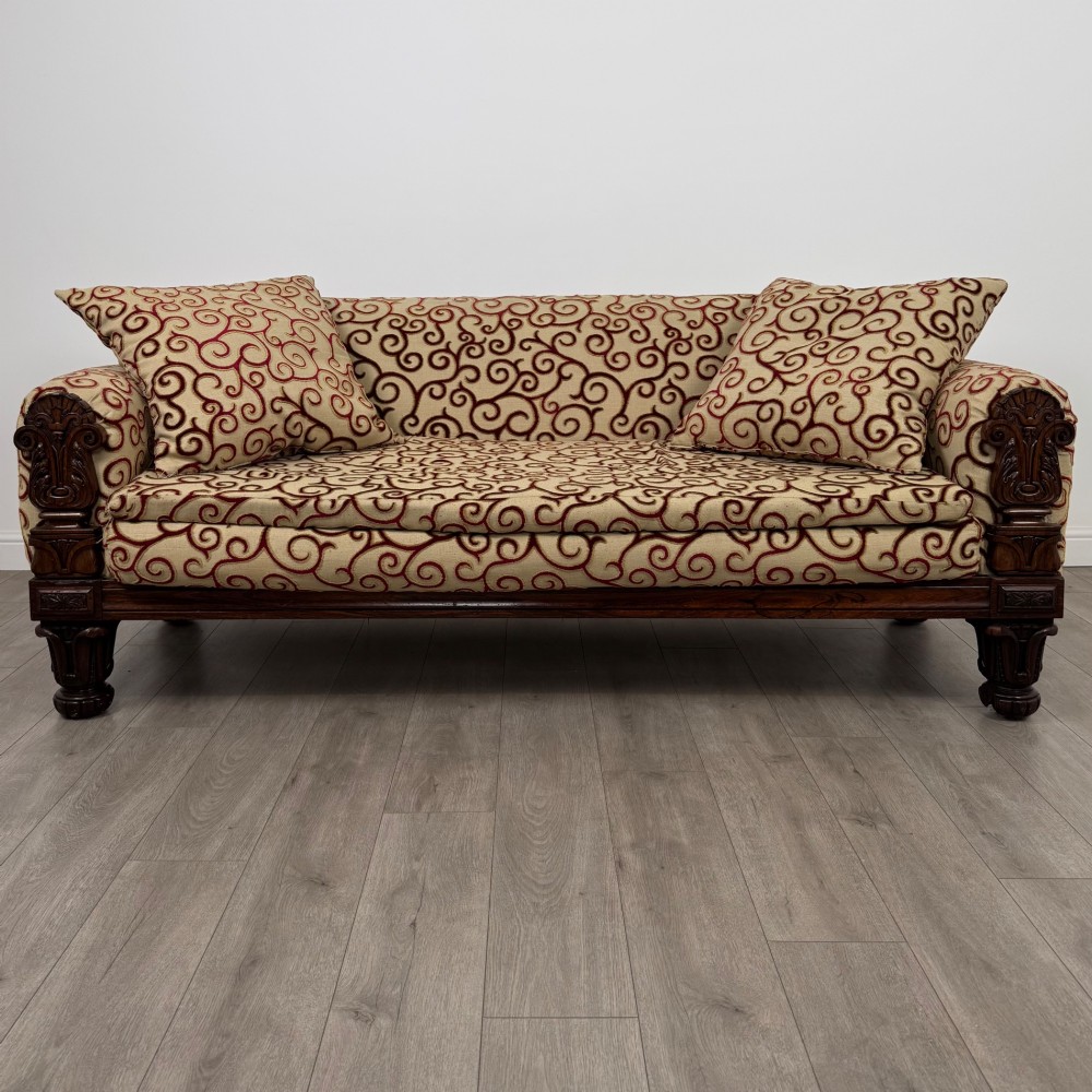 A 19th-century William IV sofa crafted from dark rosewood with carved scroll arms, turned legs, and swirl-patterned cream and burgundy fabric upholstery.