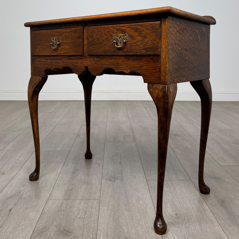 An Edwardian oak side table featuring two front drawers with brass drop handles, a scalloped apron, and slender cabriole legs. View II