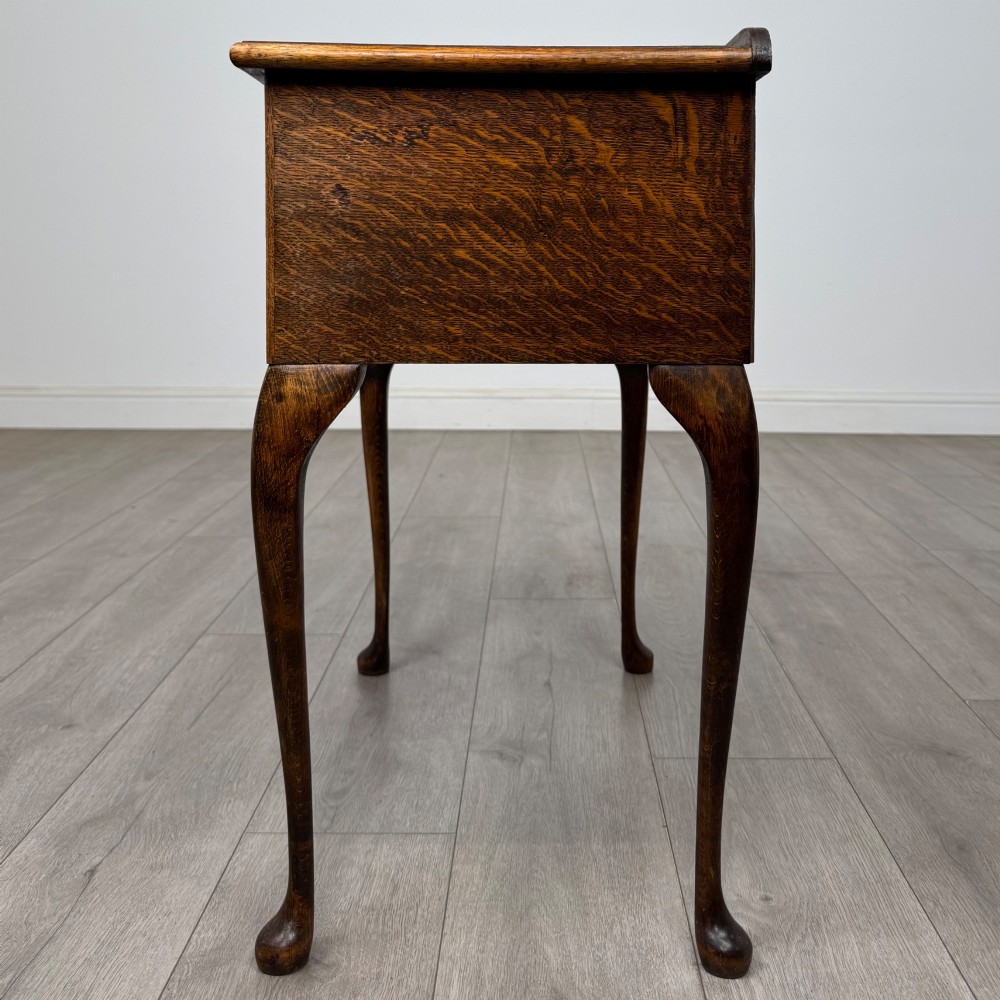 An Edwardian oak side table featuring two front drawers with brass drop handles, a scalloped apron, and slender cabriole legs. View III