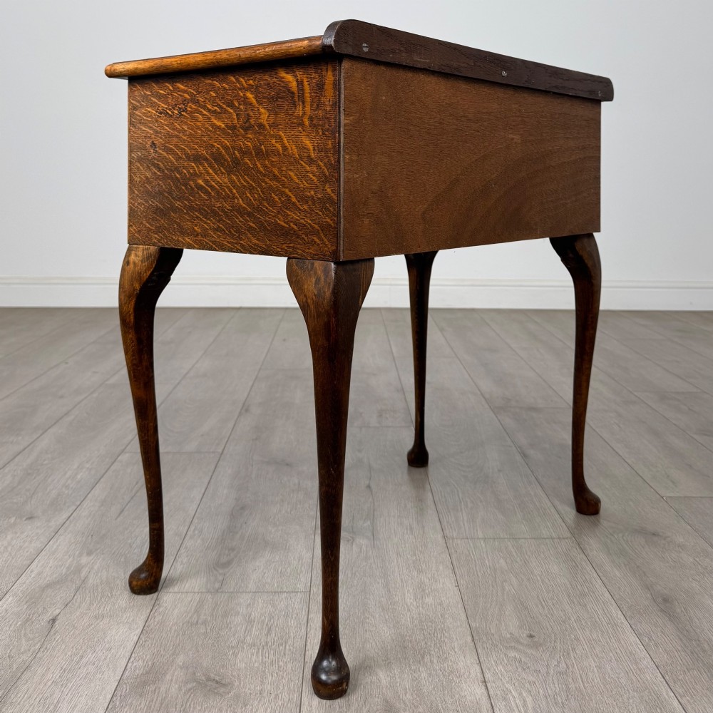 An Edwardian oak side table featuring two front drawers with brass drop handles, a scalloped apron, and slender cabriole legs. View IV