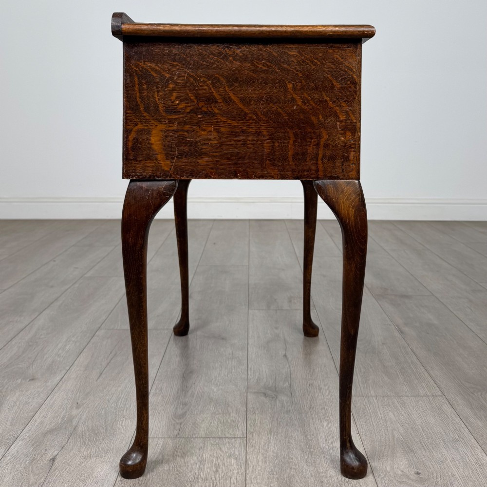 An Edwardian oak side table featuring two front drawers with brass drop handles, a scalloped apron, and slender cabriole legs. View VII