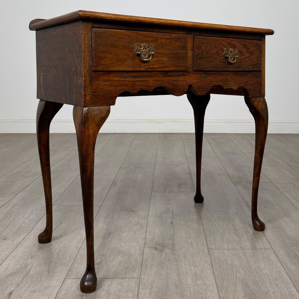 An Edwardian oak side table featuring two front drawers with brass drop handles, a scalloped apron, and slender cabriole legs. View VIII