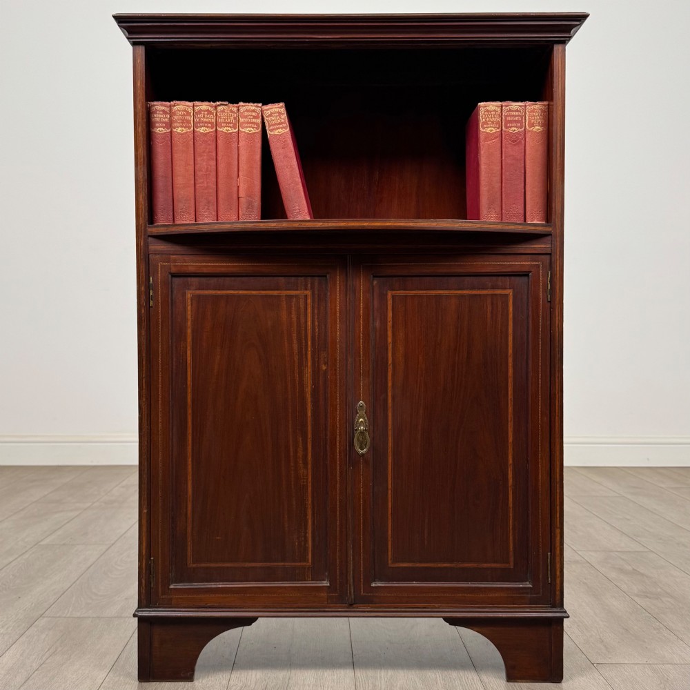 An Edwardian dark mahogany cabinet with an open upper shelf, two lower inlaid cupboard doors, and shaped bracket feet.