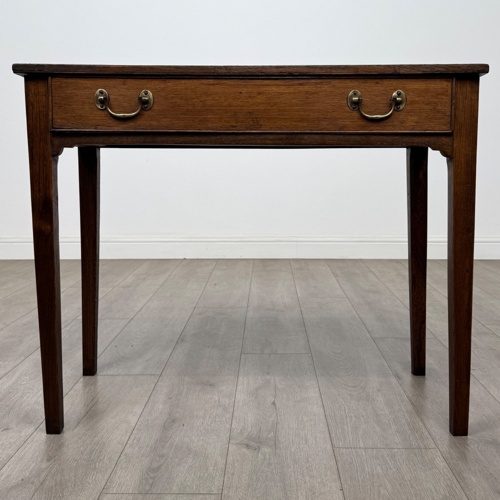 An 18th-century Georgian oak writing table with a full-width frieze drawer, two brass handles, and four square tapered legs.