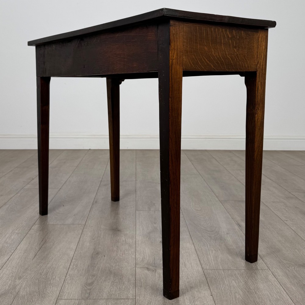 An 18th-century Georgian oak writing table with a full-width frieze drawer, two brass handles, and four square tapered legs. View VI