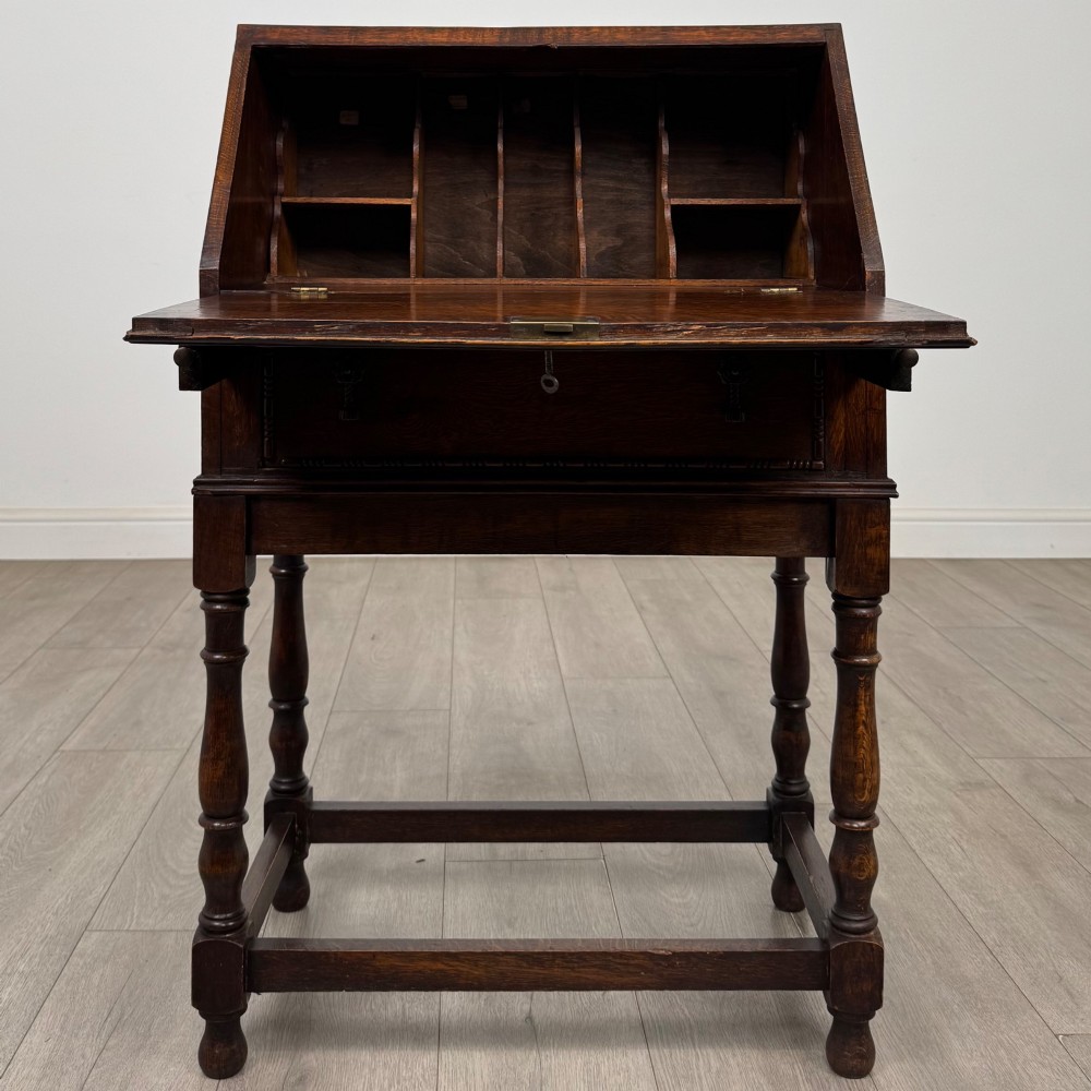 A dark oak Jacobean style bureau featuring a slanted drop-front lid, geometric moulding, a single drawer with teardrop handles, and turned legs with low stretchers. View II