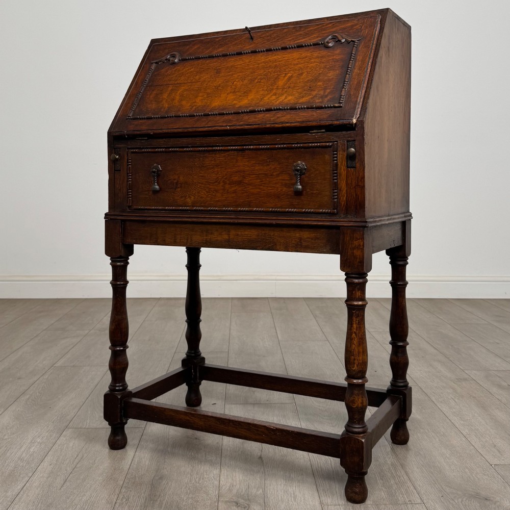 A dark oak Jacobean style bureau featuring a slanted drop-front lid, geometric moulding, a single drawer with teardrop handles, and turned legs with low stretchers. View III