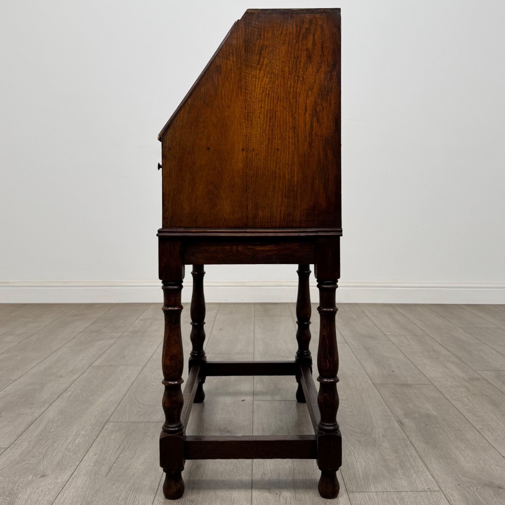 A dark oak Jacobean style bureau featuring a slanted drop-front lid, geometric moulding, a single drawer with teardrop handles, and turned legs with low stretchers. View IV