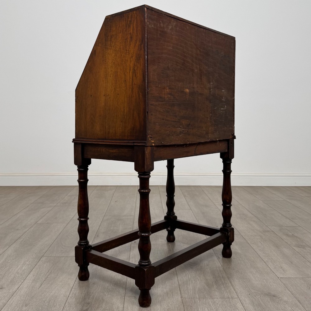 A dark oak Jacobean style bureau featuring a slanted drop-front lid, geometric moulding, a single drawer with teardrop handles, and turned legs with low stretchers. View V