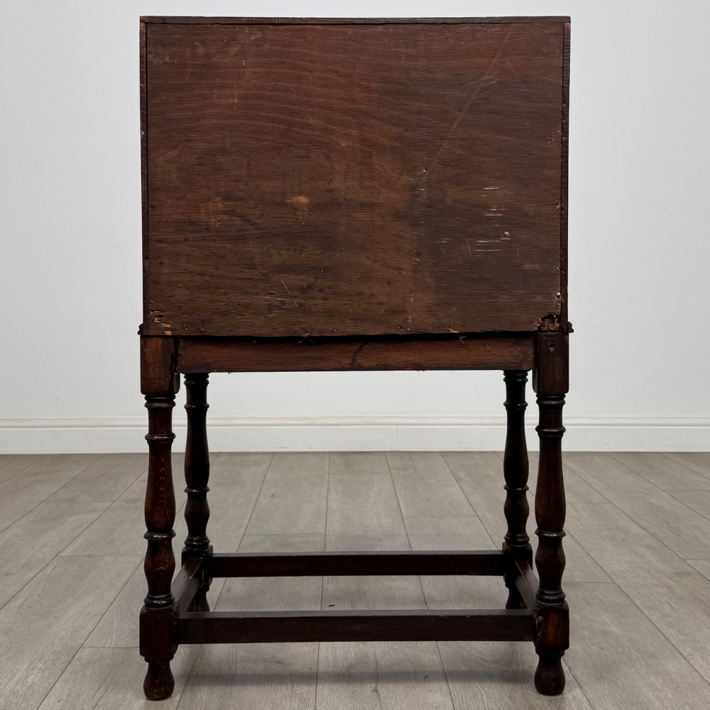 A dark oak Jacobean style bureau featuring a slanted drop-front lid, geometric moulding, a single drawer with teardrop handles, and turned legs with low stretchers. View VI