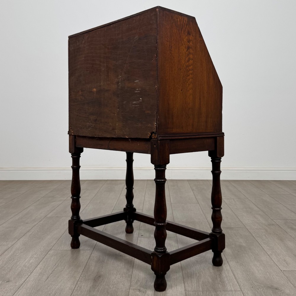 A dark oak Jacobean style bureau featuring a slanted drop-front lid, geometric moulding, a single drawer with teardrop handles, and turned legs with low stretchers. View VII