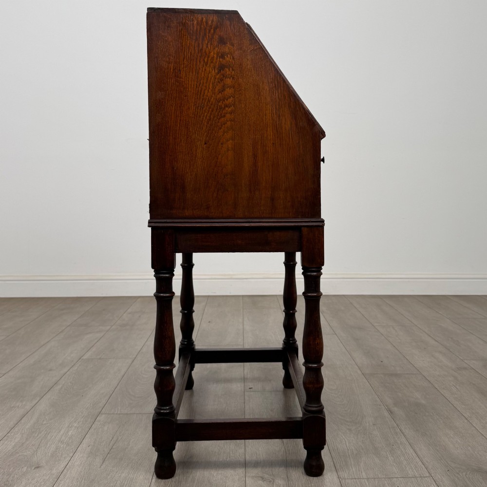 A dark oak Jacobean style bureau featuring a slanted drop-front lid, geometric moulding, a single drawer with teardrop handles, and turned legs with low stretchers. View VIII