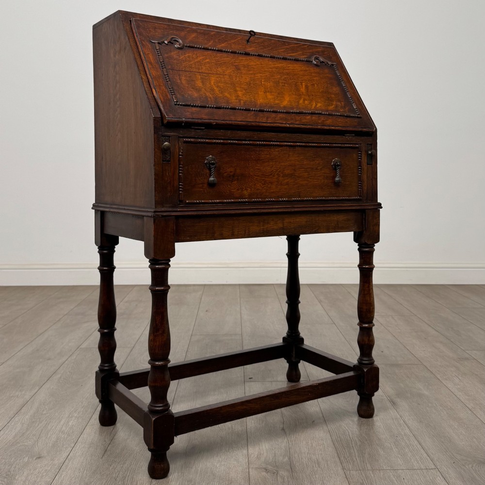 A dark oak Jacobean style bureau featuring a slanted drop-front lid, geometric moulding, a single drawer with teardrop handles, and turned legs with low stretchers. View IX