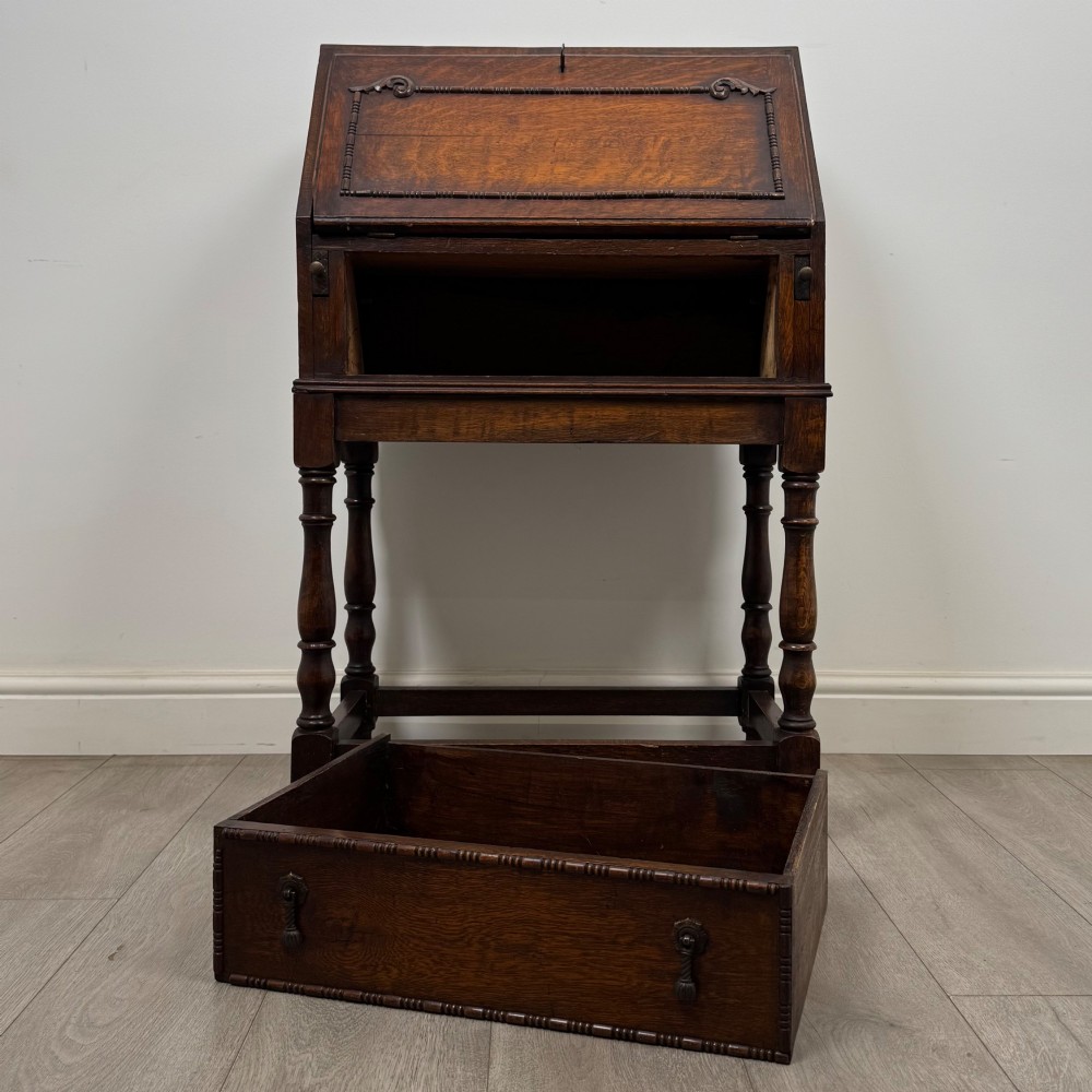 A dark oak Jacobean style bureau featuring a slanted drop-front lid, geometric moulding, a single drawer with teardrop handles, and turned legs with low stretchers. View XII