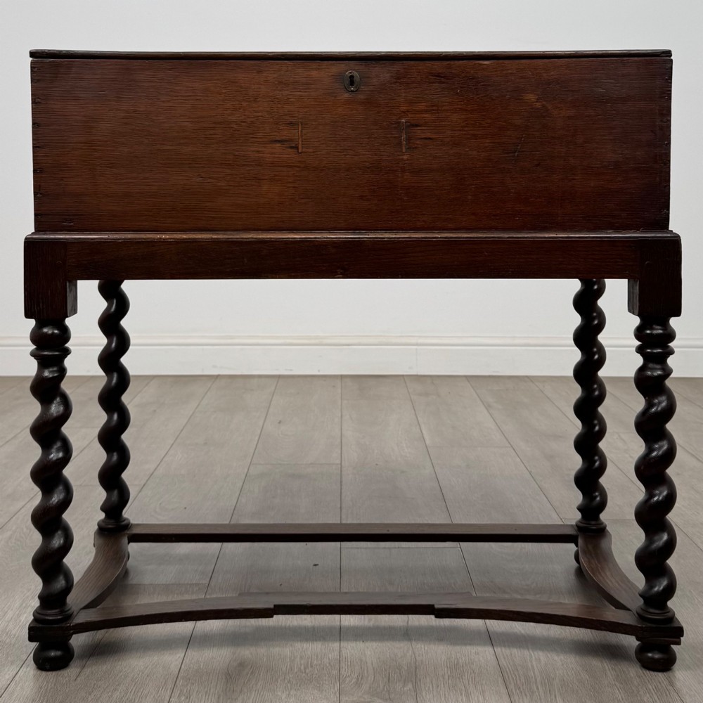 A 19th-century dark oak box on a wooden stand featuring four spiral barley twist legs and a central brass keyhole escutcheon.