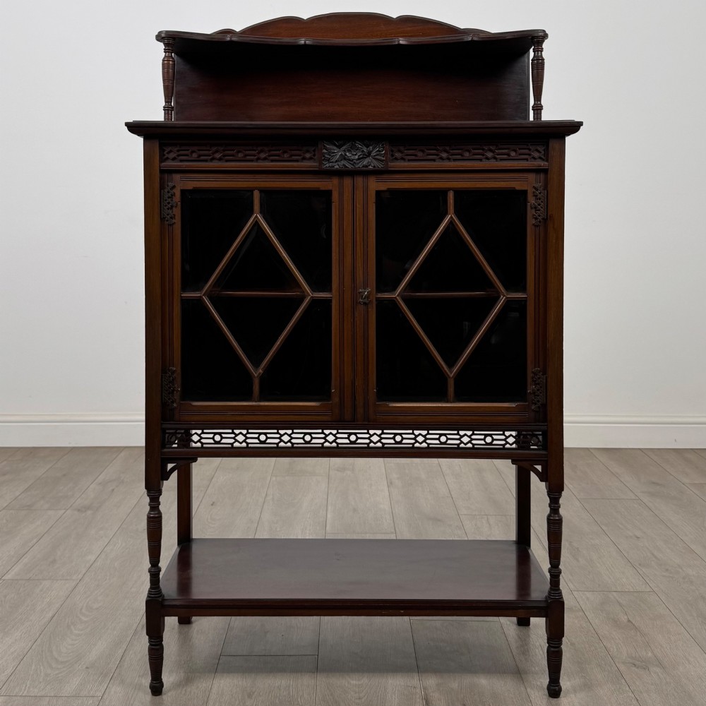 An Edwardian mahogany display cabinet featuring twin diamond-glazed doors, an upper shelf gallery, decorative fretwork, turned support legs, and an undertier.