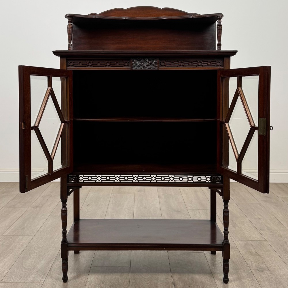 An Edwardian mahogany display cabinet featuring twin diamond-glazed doors, an upper shelf gallery, decorative fretwork, turned support legs, and an undertier. View II