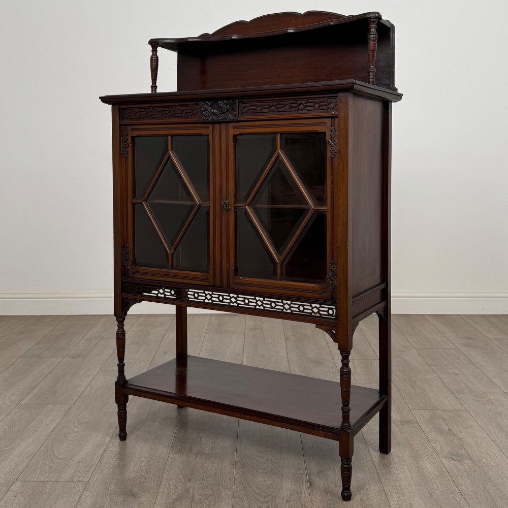 An Edwardian mahogany display cabinet featuring twin diamond-glazed doors, an upper shelf gallery, decorative fretwork, turned support legs, and an undertier. View III
