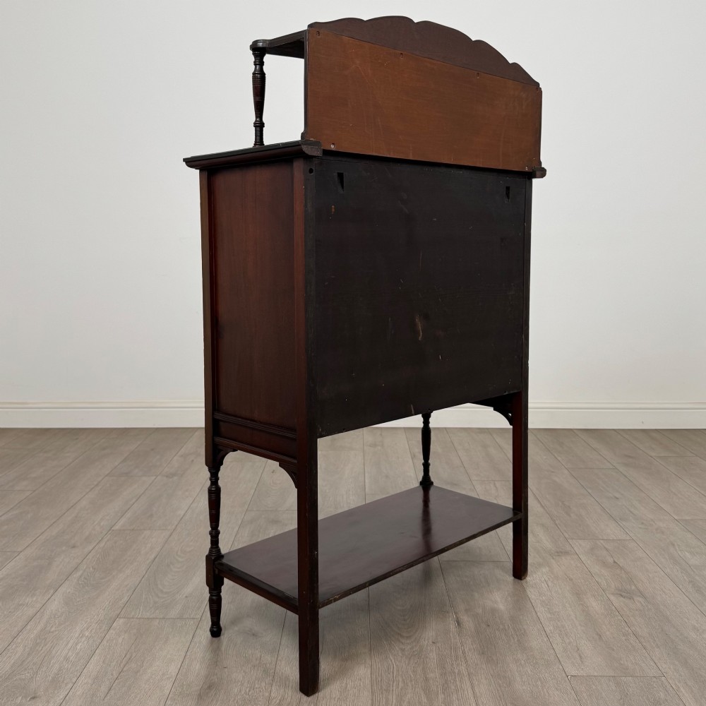 An Edwardian mahogany display cabinet featuring twin diamond-glazed doors, an upper shelf gallery, decorative fretwork, turned support legs, and an undertier. View V