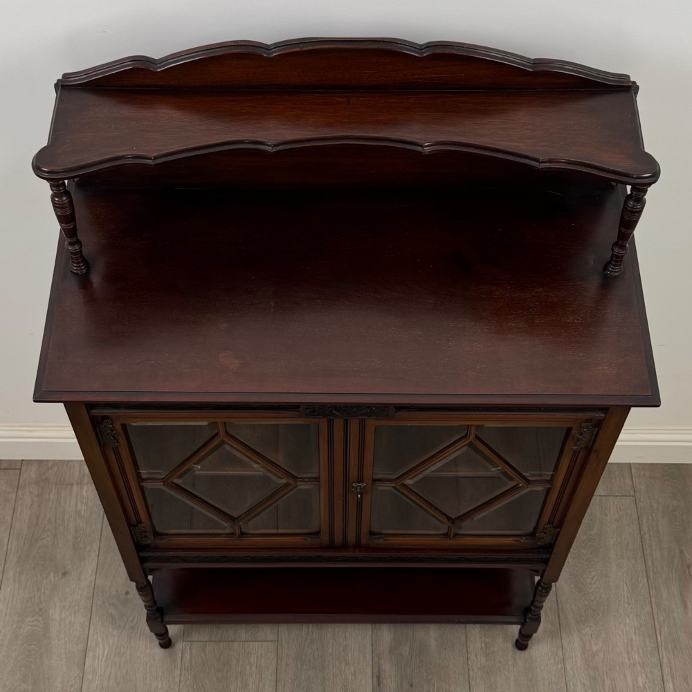 An Edwardian mahogany display cabinet featuring twin diamond-glazed doors, an upper shelf gallery, decorative fretwork, turned support legs, and an undertier. View X