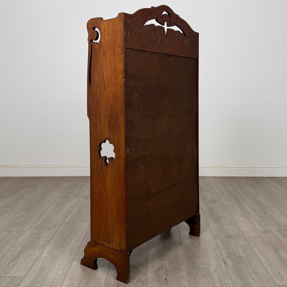 An antique Arts and Crafts oak writing bureau featuring a slant drop-front desk, a pierced cresting top rail, dark iron strap hardware, an open shelf, and lower double doors. View VI