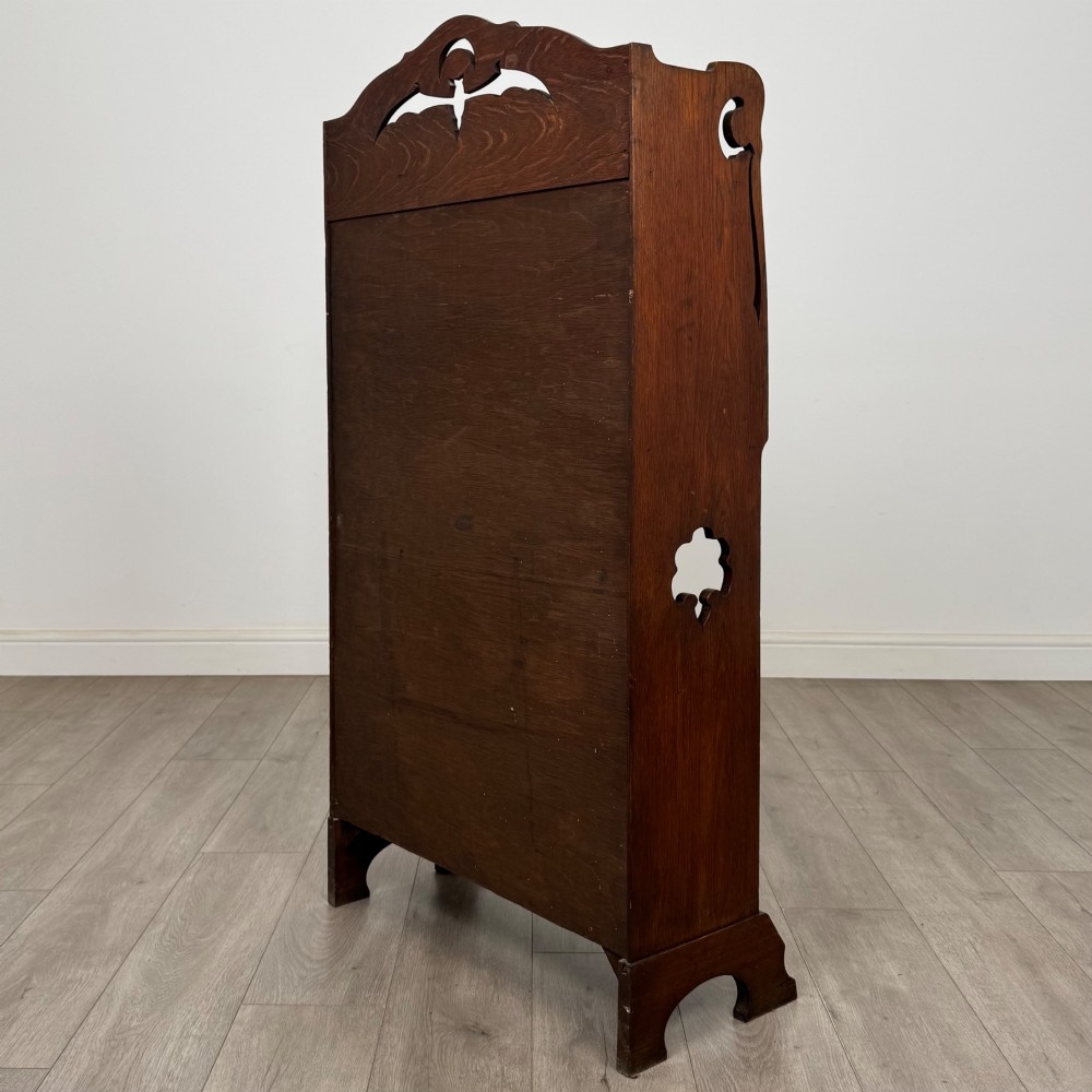 An antique Arts and Crafts oak writing bureau featuring a slant drop-front desk, a pierced cresting top rail, dark iron strap hardware, an open shelf, and lower double doors. View VIII
