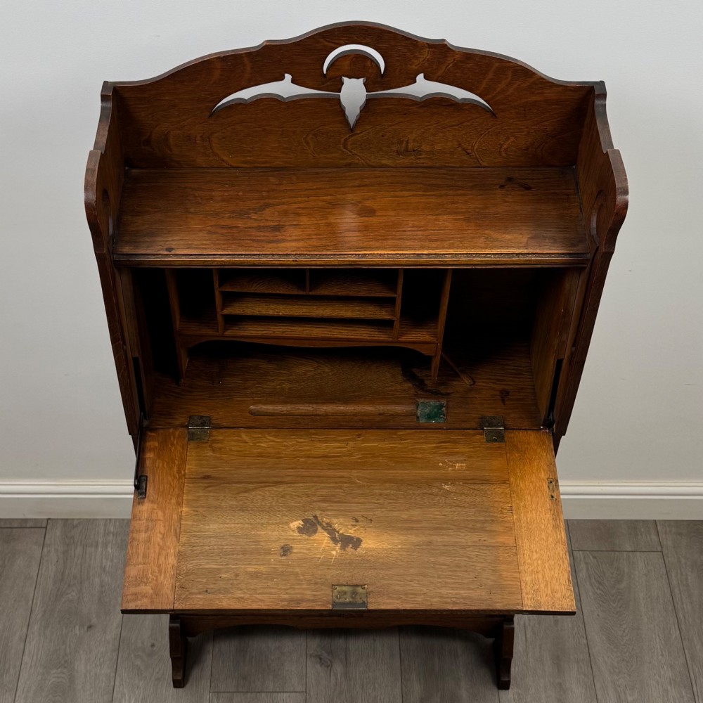 An antique Arts and Crafts oak writing bureau featuring a slant drop-front desk, a pierced cresting top rail, dark iron strap hardware, an open shelf, and lower double doors. View XII