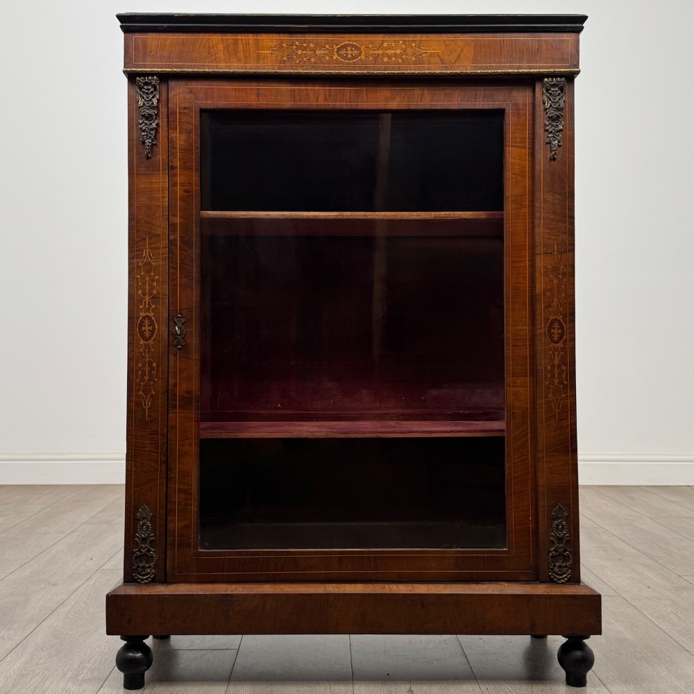 A 19th-century Victorian walnut pier cabinet featuring floral marquetry inlays, gilded metal mounts, and a single glazed door revealing interior shelves.