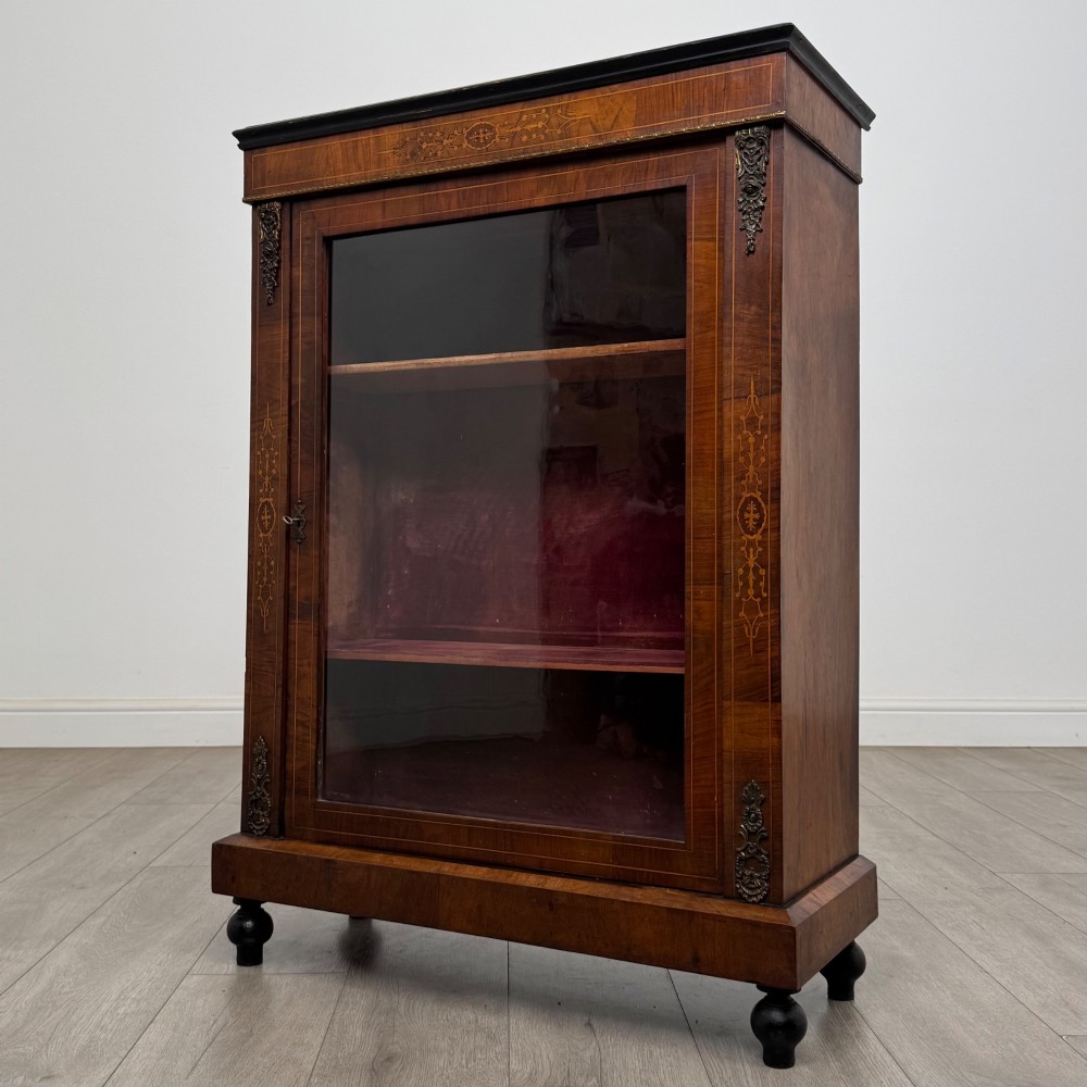 A 19th-century Victorian walnut pier cabinet featuring floral marquetry inlays, gilded metal mounts, and a single glazed door revealing interior shelves. View III