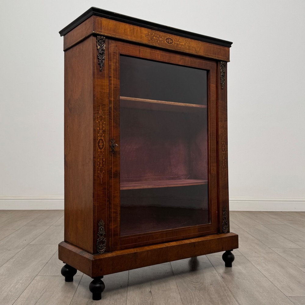 A 19th-century Victorian walnut pier cabinet featuring floral marquetry inlays, gilded metal mounts, and a single glazed door revealing interior shelves. View IX