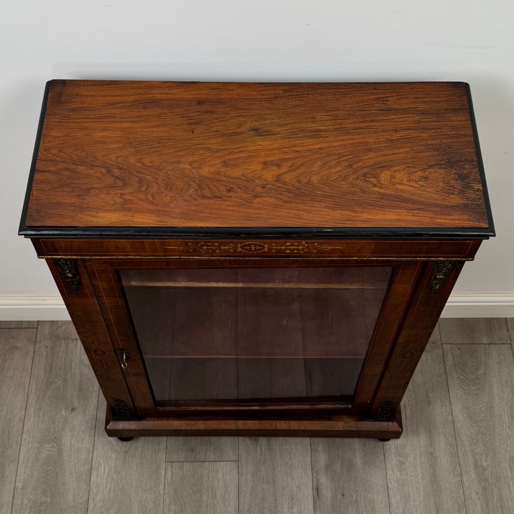 A 19th-century Victorian walnut pier cabinet featuring floral marquetry inlays, gilded metal mounts, and a single glazed door revealing interior shelves. View X