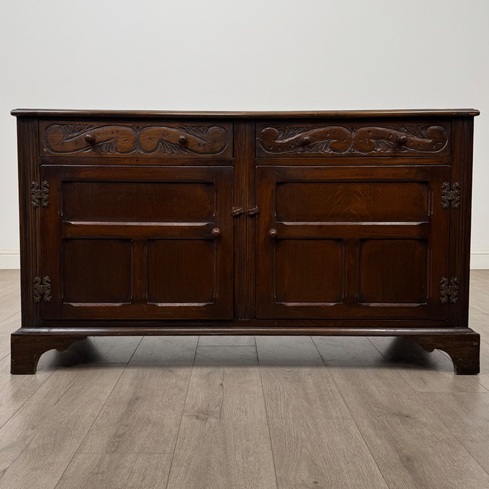 A dark oak sideboard featuring two carved upper drawers above panelled cupboard doors with decorative iron hinges and wooden knobs.
