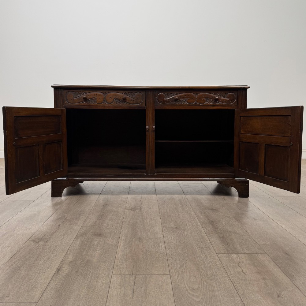 A dark oak sideboard featuring two carved upper drawers above panelled cupboard doors with decorative iron hinges and wooden knobs. View II