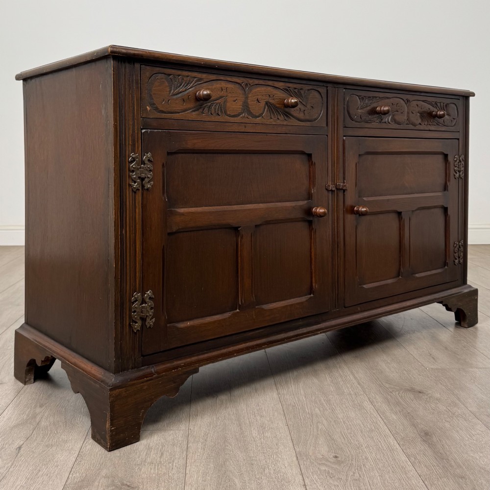 A dark oak sideboard featuring two carved upper drawers above panelled cupboard doors with decorative iron hinges and wooden knobs. View IX