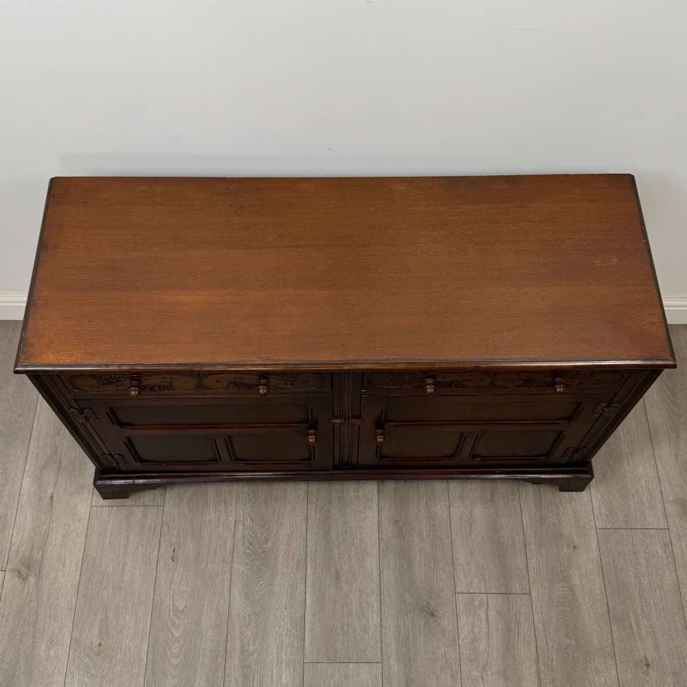 A dark oak sideboard featuring two carved upper drawers above panelled cupboard doors with decorative iron hinges and wooden knobs. View X