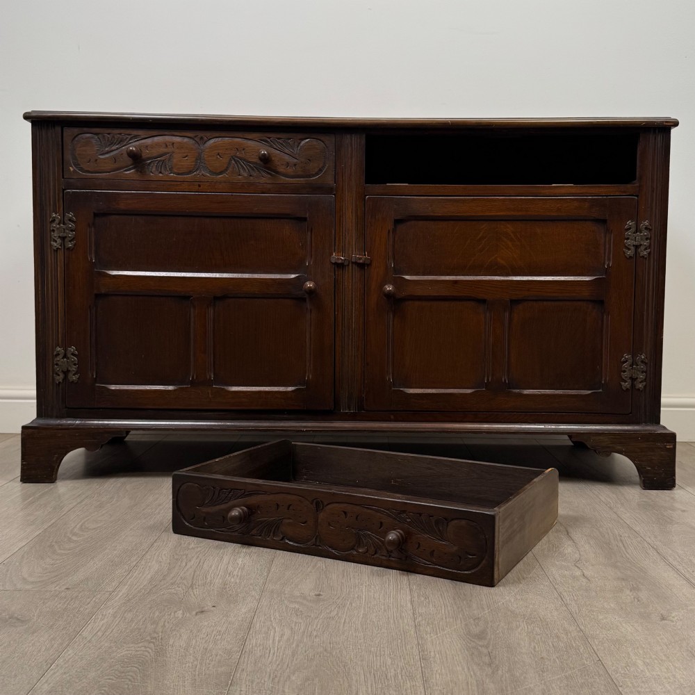 A dark oak sideboard featuring two carved upper drawers above panelled cupboard doors with decorative iron hinges and wooden knobs. View XI