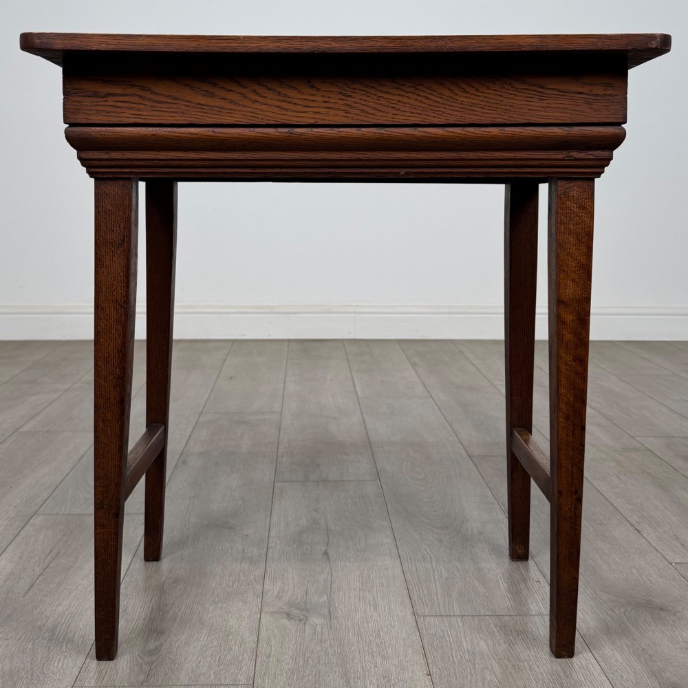 An Edwardian oak side table featuring a rectangular top, moulded frieze, tapered square legs, and low side stretchers.