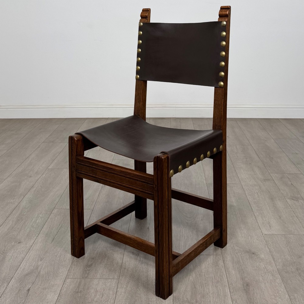 A set of six dark oak dining chairs featuring thick dark brown leather sling backrests and seats secured with decorative brass studs. View II
