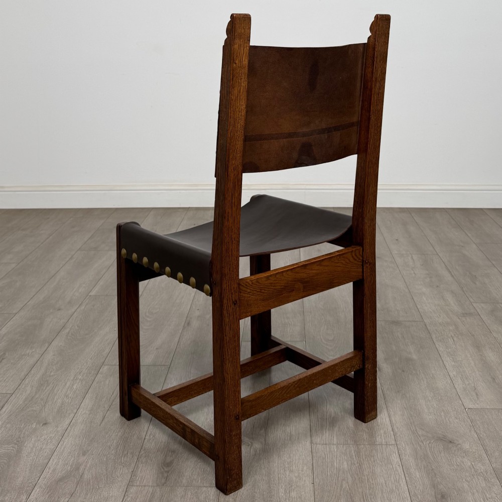 A set of six dark oak dining chairs featuring thick dark brown leather sling backrests and seats secured with decorative brass studs. View III