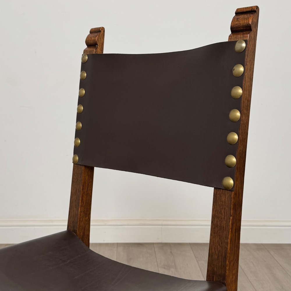 A set of six dark oak dining chairs featuring thick dark brown leather sling backrests and seats secured with decorative brass studs. View IV