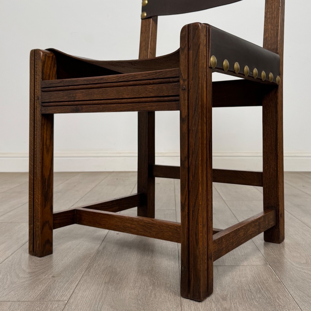 A set of six dark oak dining chairs featuring thick dark brown leather sling backrests and seats secured with decorative brass studs. View V