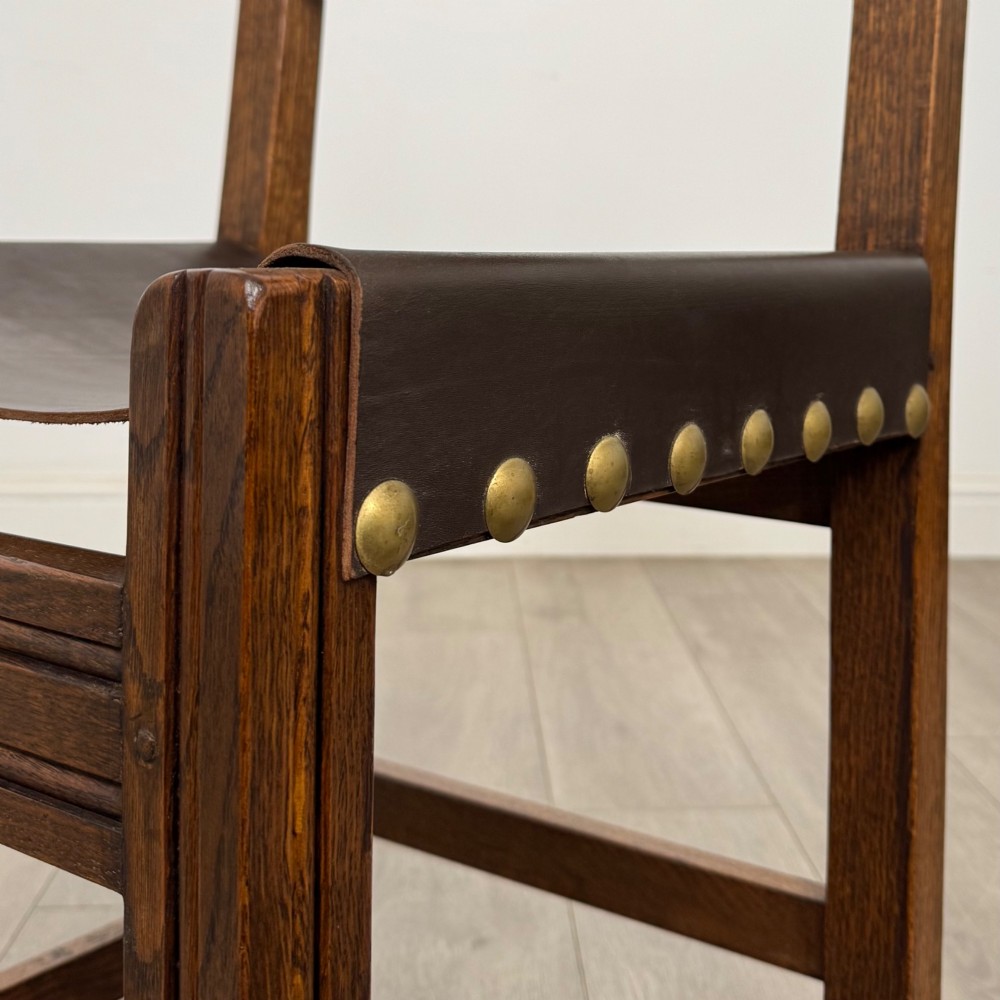 A set of six dark oak dining chairs featuring thick dark brown leather sling backrests and seats secured with decorative brass studs. View VI