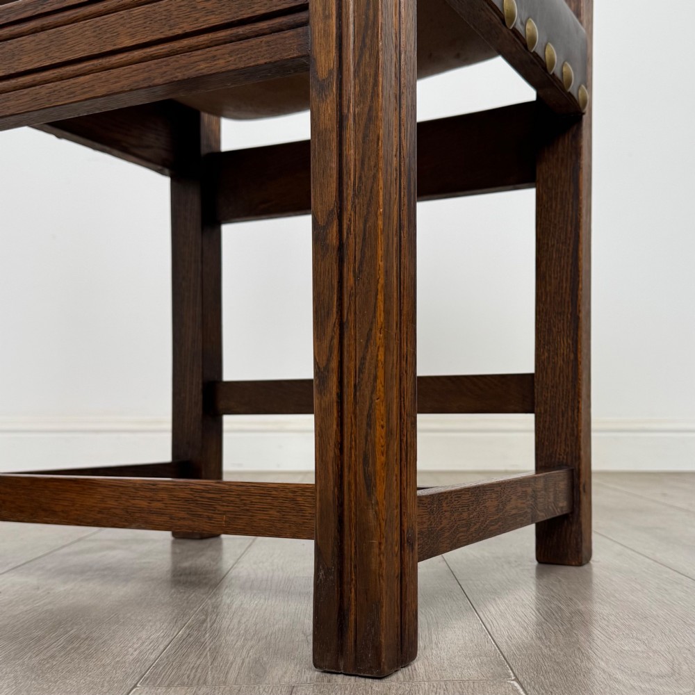 A set of six dark oak dining chairs featuring thick dark brown leather sling backrests and seats secured with decorative brass studs. View VII