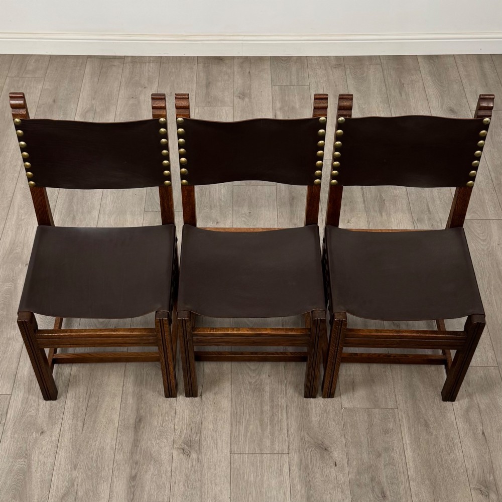 A set of six dark oak dining chairs featuring thick dark brown leather sling backrests and seats secured with decorative brass studs. View VIII